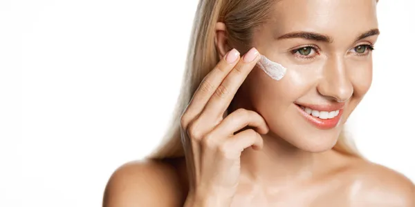 Uśmiechnięta młoda kobieta aplikuje kremowe serum na twarz